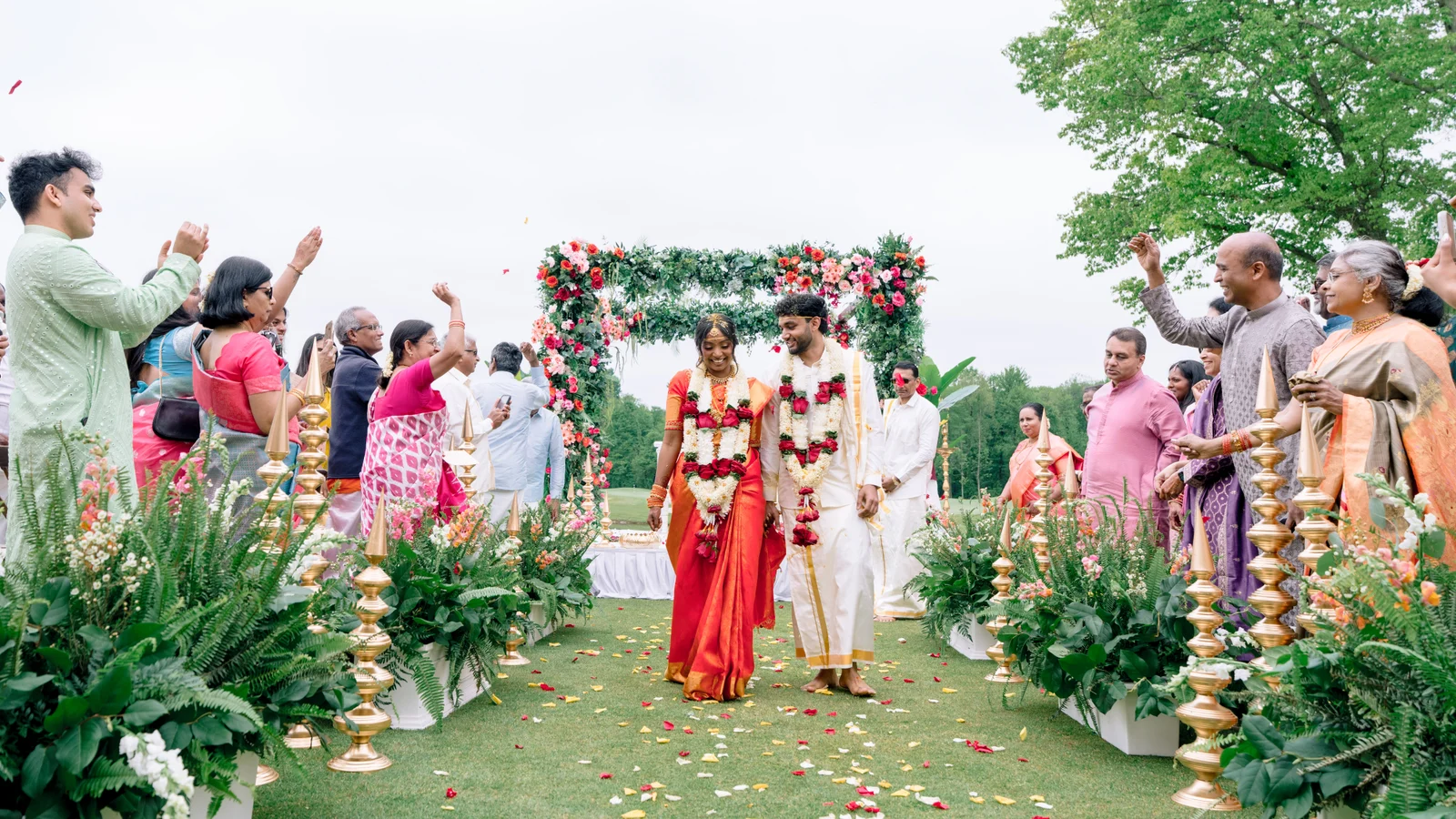 Newlyweds walking down a flower-lined aisle surrounded by their guests